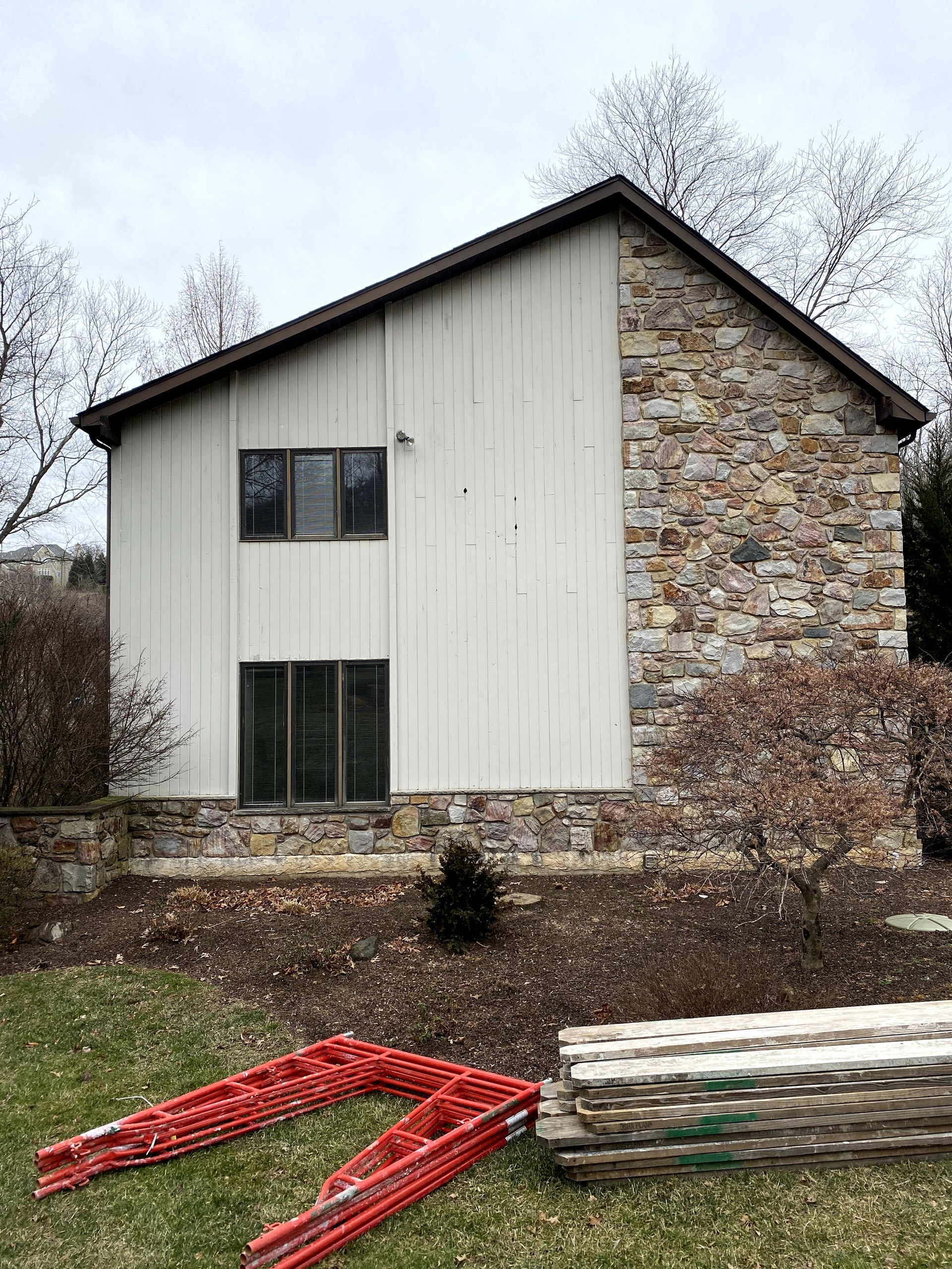 A white house with a stone wall and a ladder in front of it.