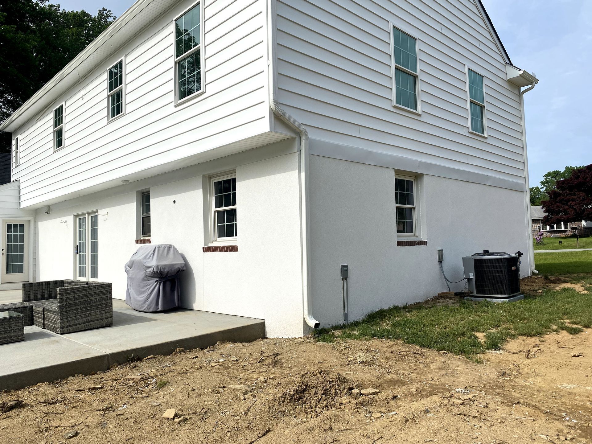 A white house with a patio and a grill in the backyard.