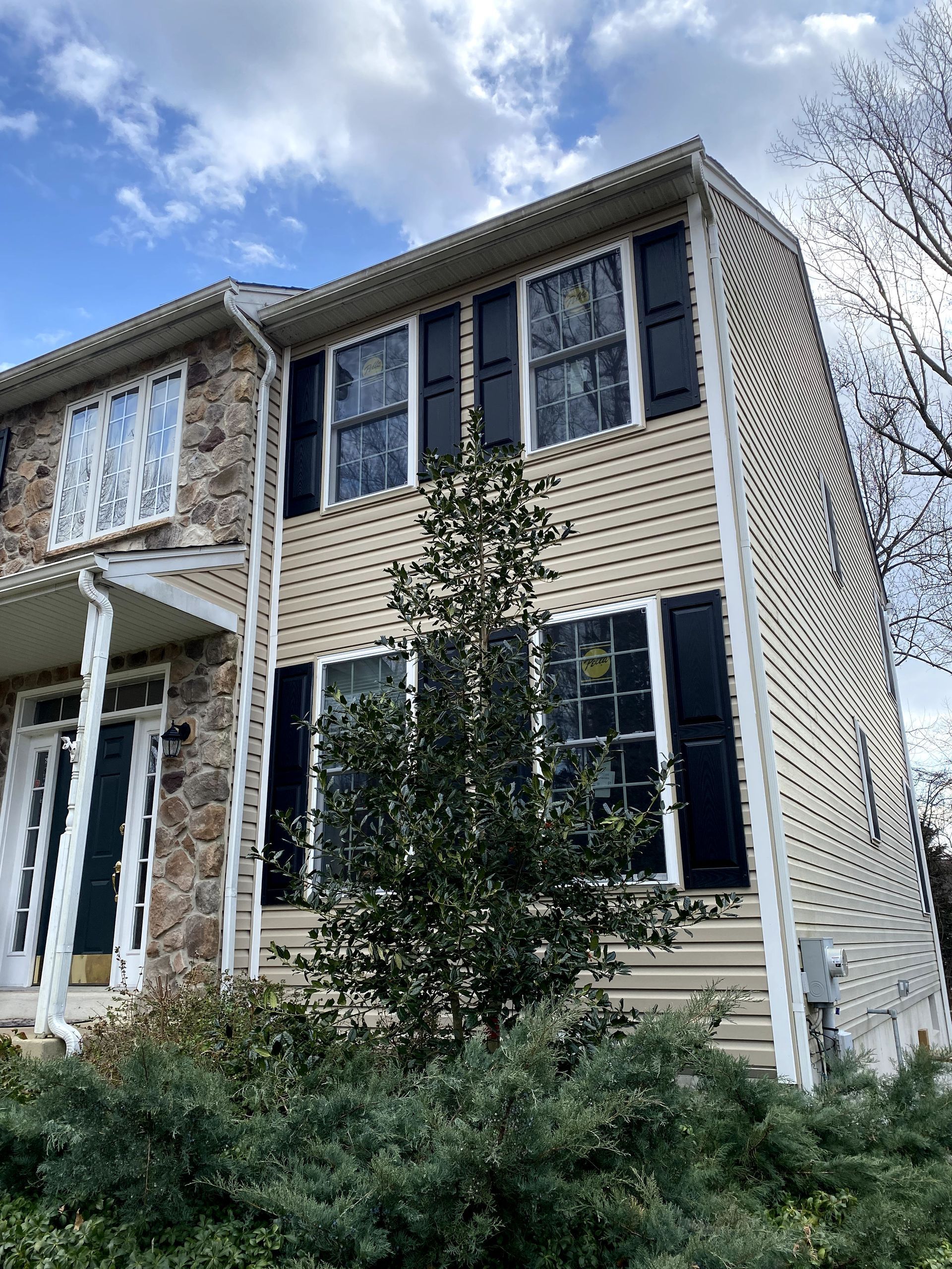 A house with black shutters and a tree in front of it.