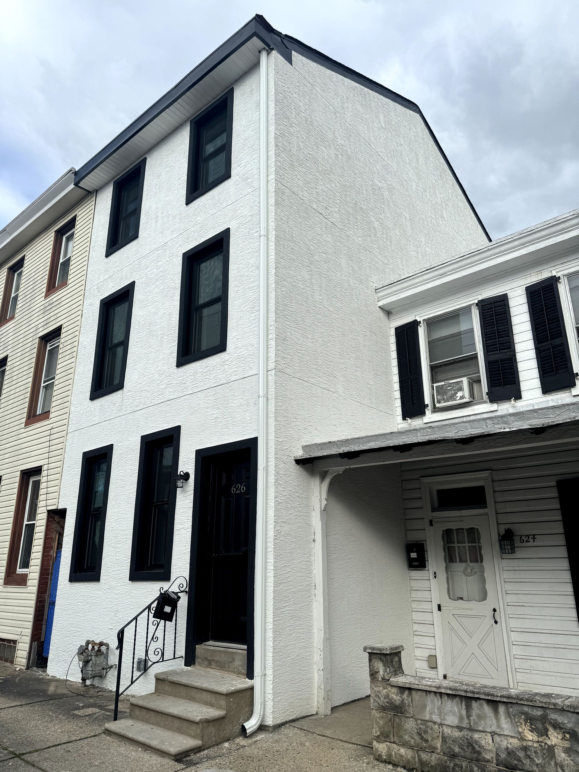 A white building with black windows and shutters on a cloudy day.