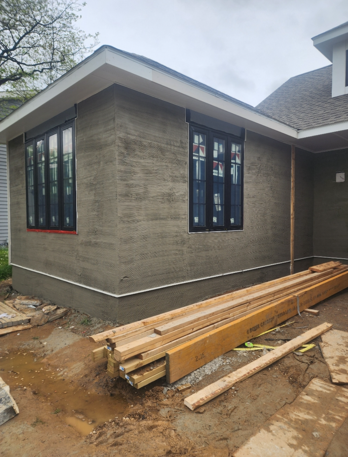 A house under construction with a stack of wood in front of it.