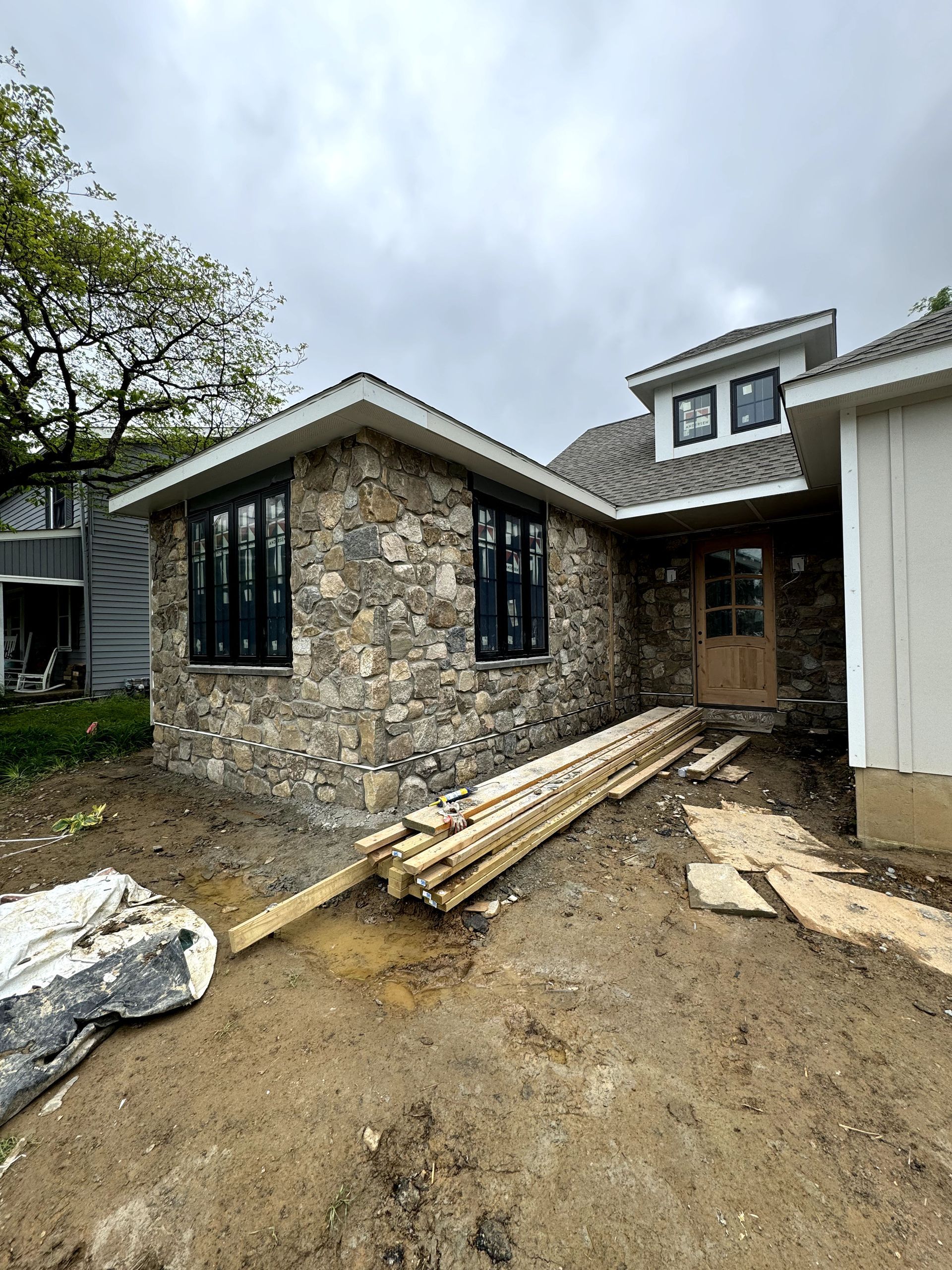 A large stone house is being built with a lot of wood in front of it.