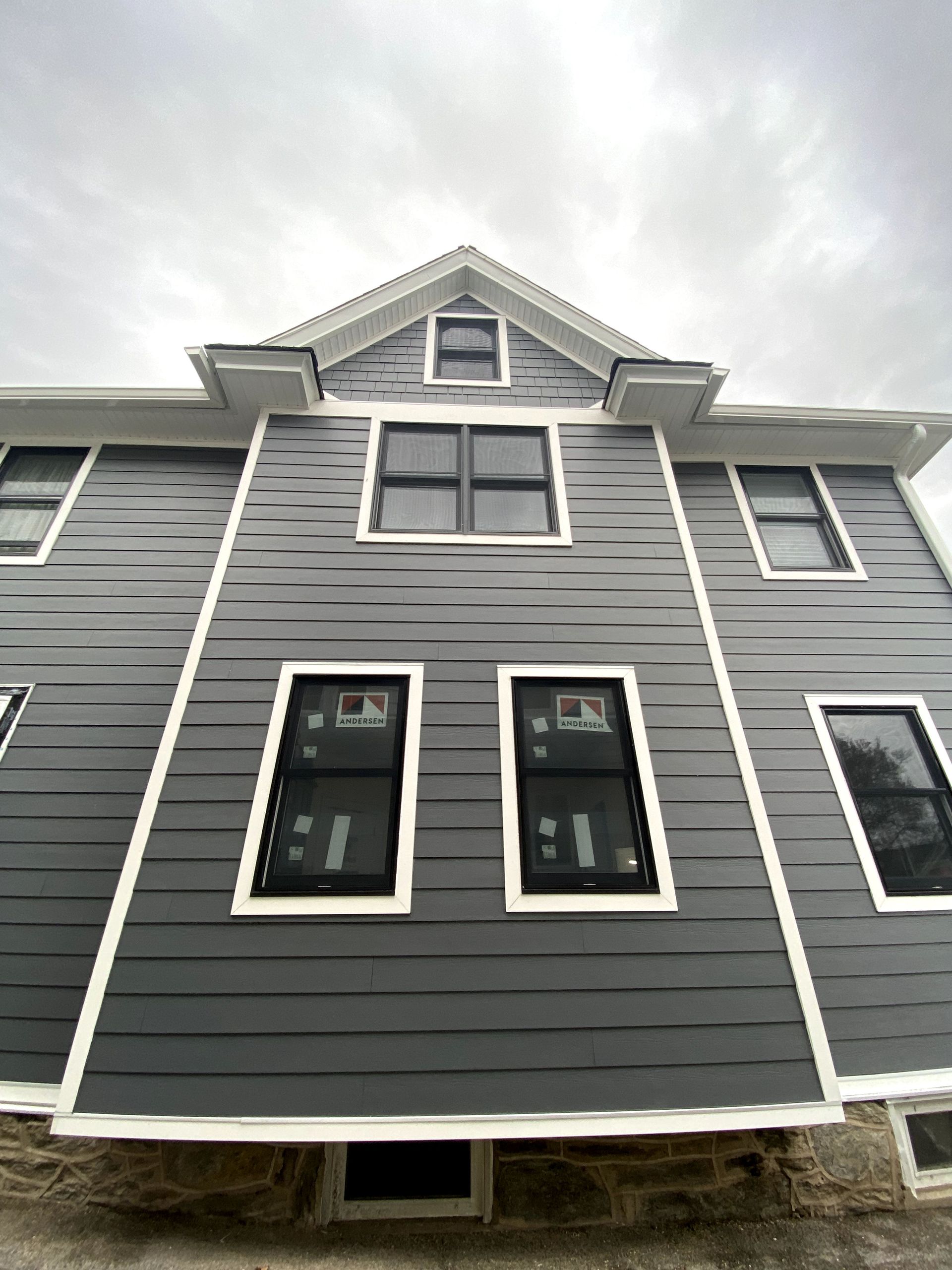 A large gray house with a lot of windows and a cloudy sky in the background.