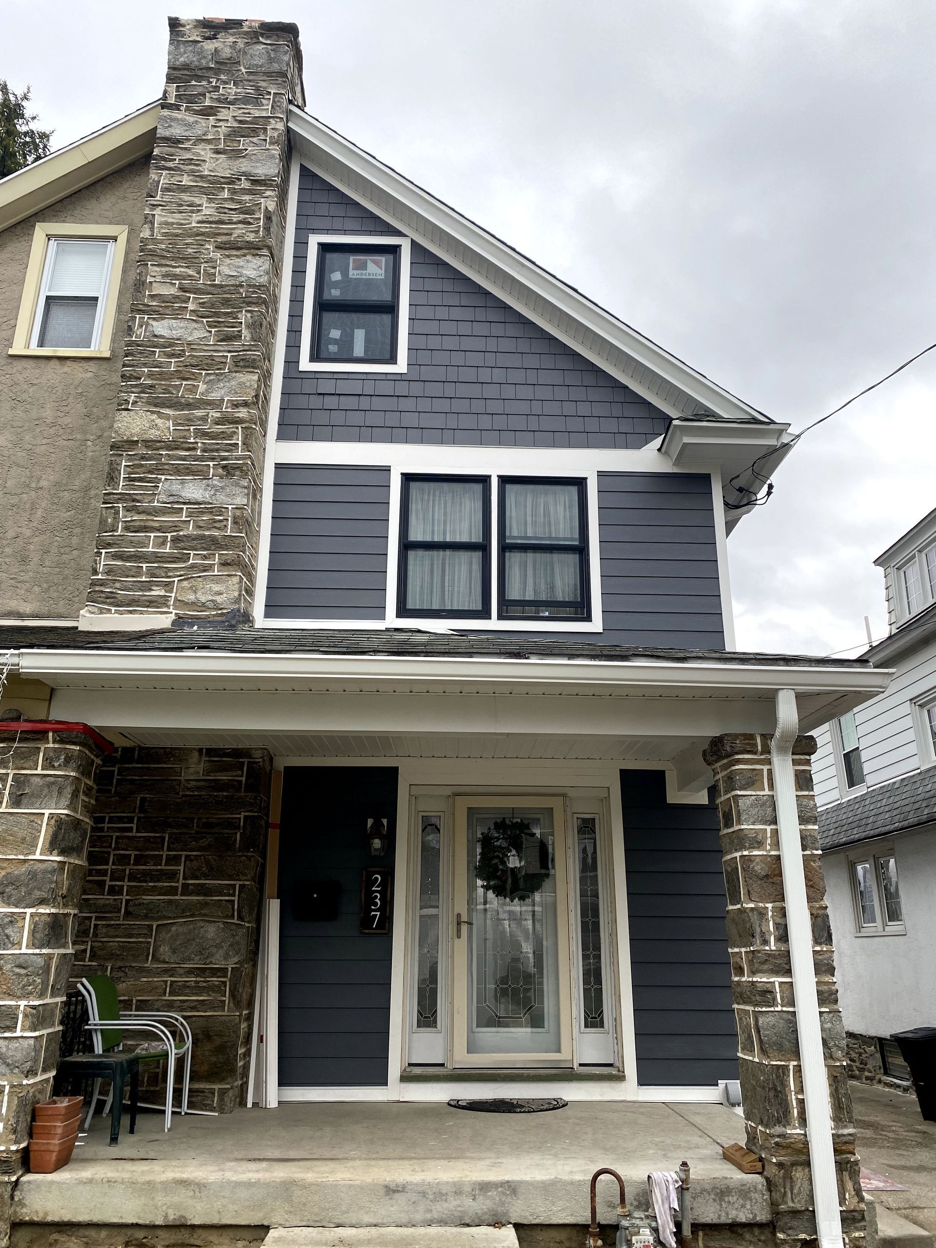The front of a house with a stone chimney and a blue siding.