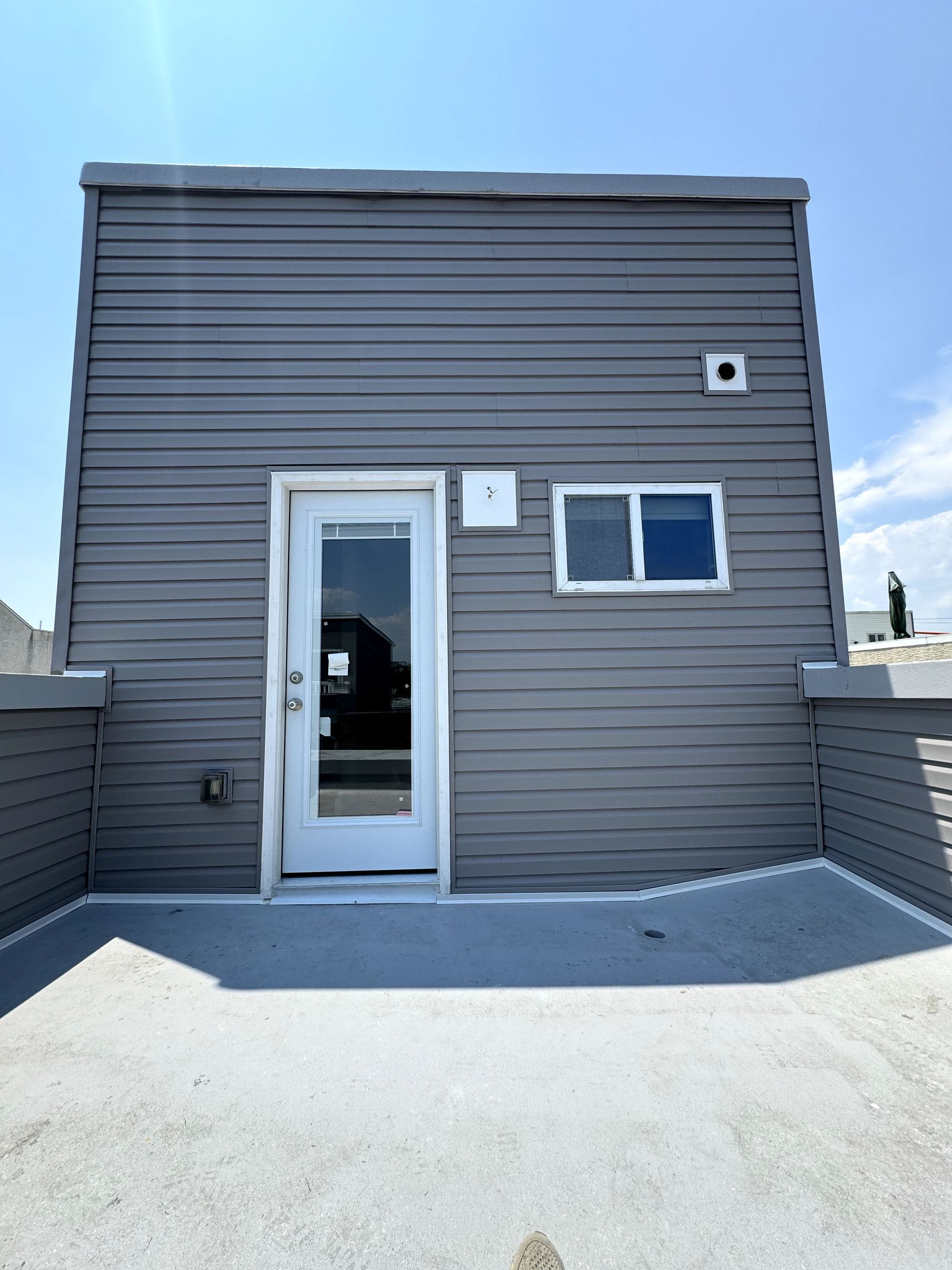 A gray building with a white door and two windows