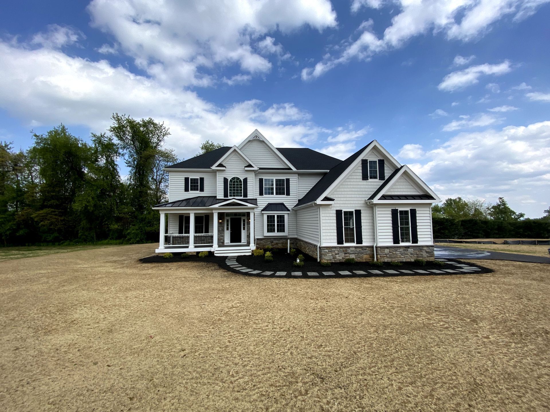 A large white house with a black roof is sitting on top of a dirt field.