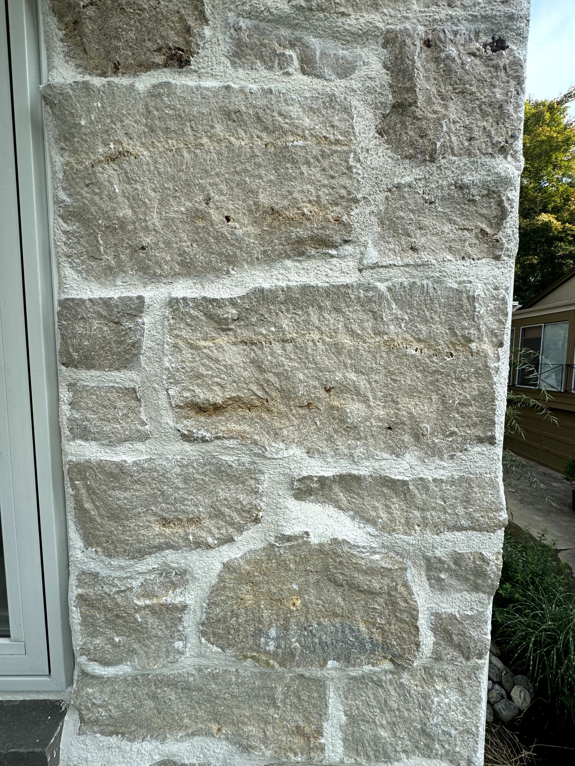 A close up of a stone wall with a window in the background.