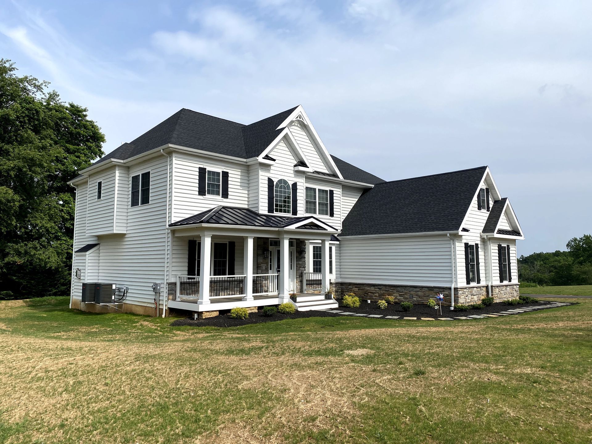 A large white house with a black roof is sitting in the middle of a grassy field.