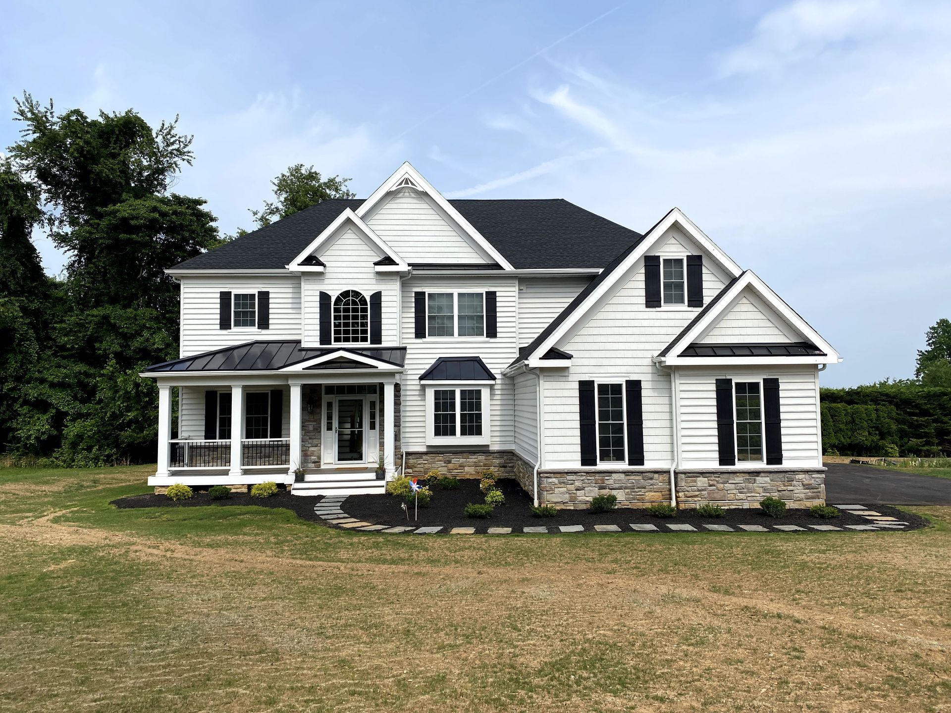 A large white house with black shutters is sitting on top of a lush green field.