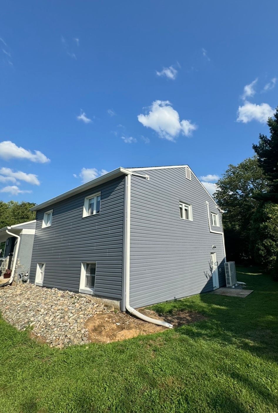 A large house with a gray siding is sitting on top of a lush green field.