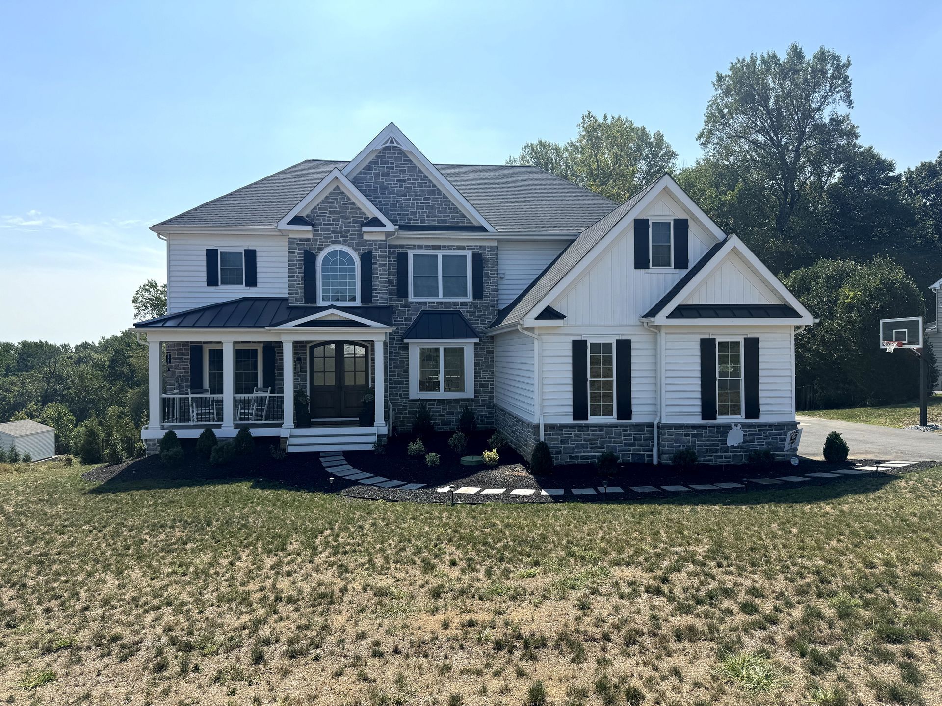 A large white house with black shutters is sitting in the middle of a grassy field.