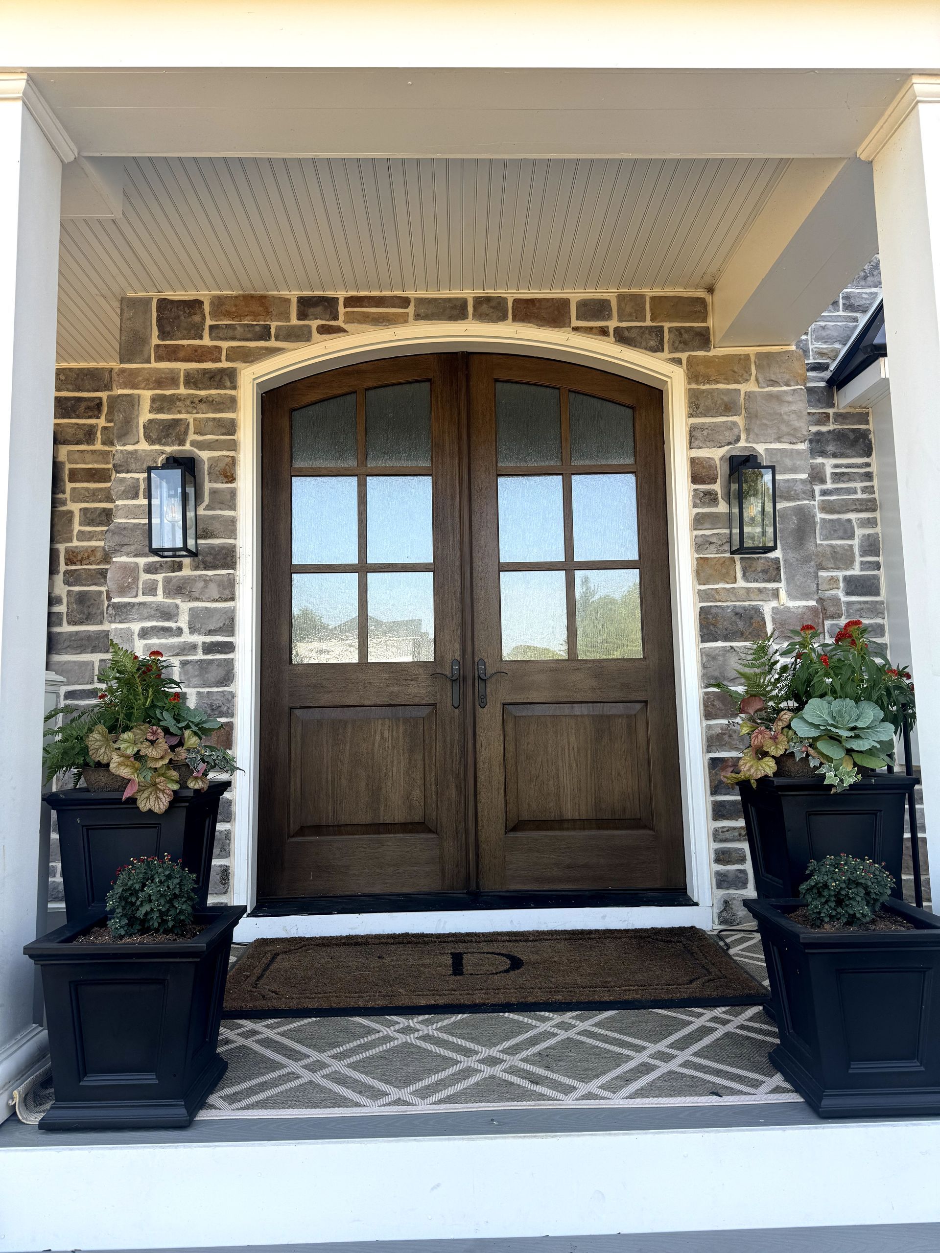 The front door of a brick house with a wooden door and potted plants.