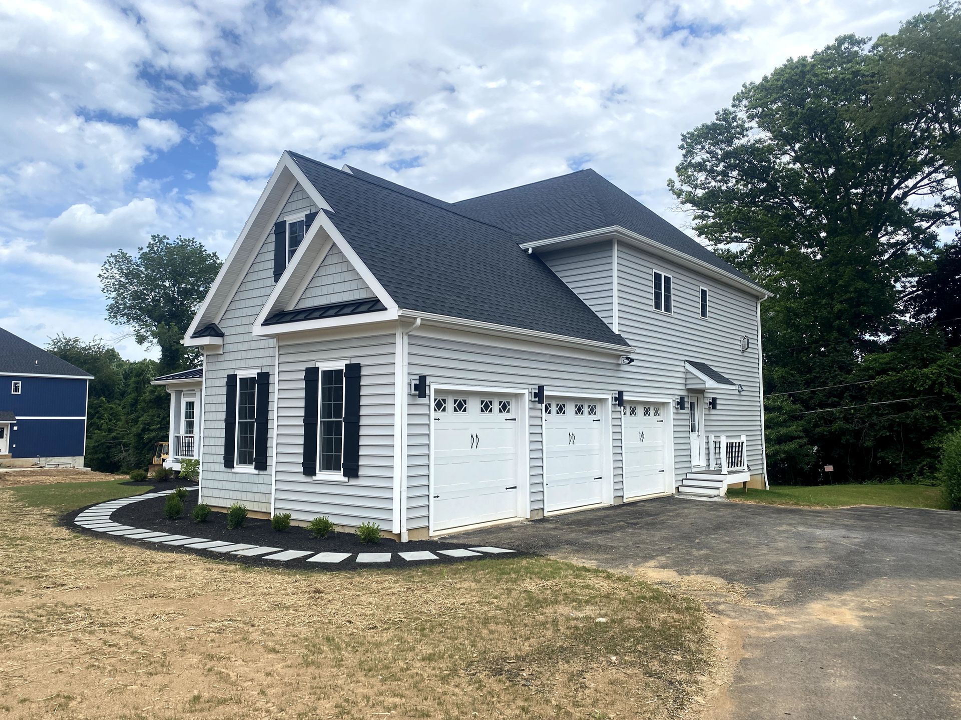 A white house with a black roof and white garage doors.