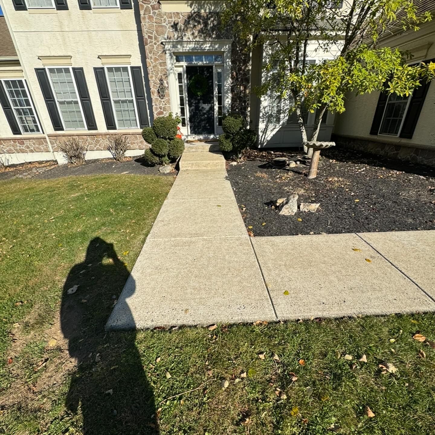 A shadow of a person is cast on a sidewalk in front of a house.
