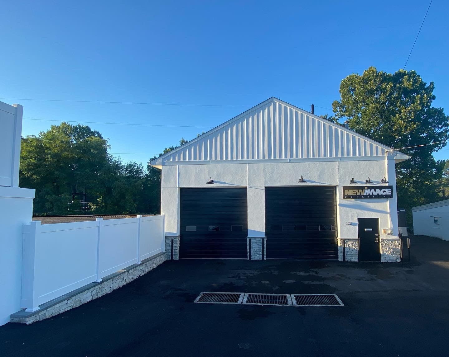 A white garage with two black garage doors and a white fence.