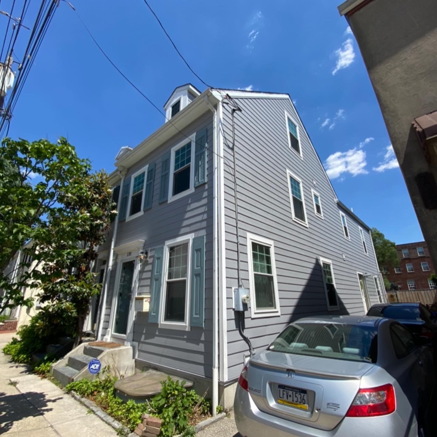 A silver car is parked in front of a grey house