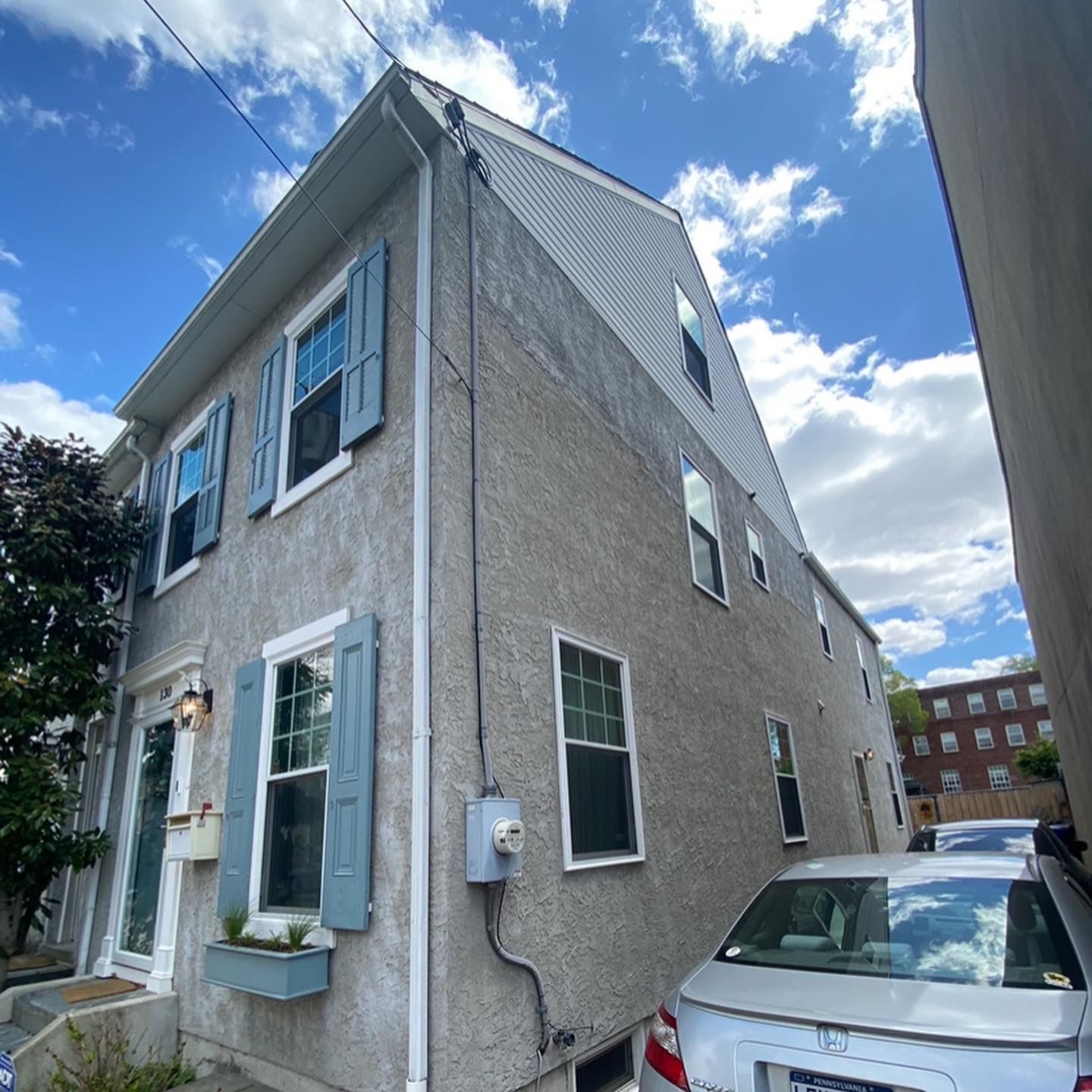 A white car is parked in front of a house with blue shutters