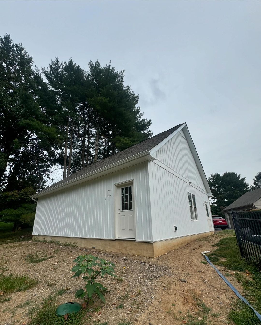 A white garage with a black roof is sitting in the middle of a dirt field