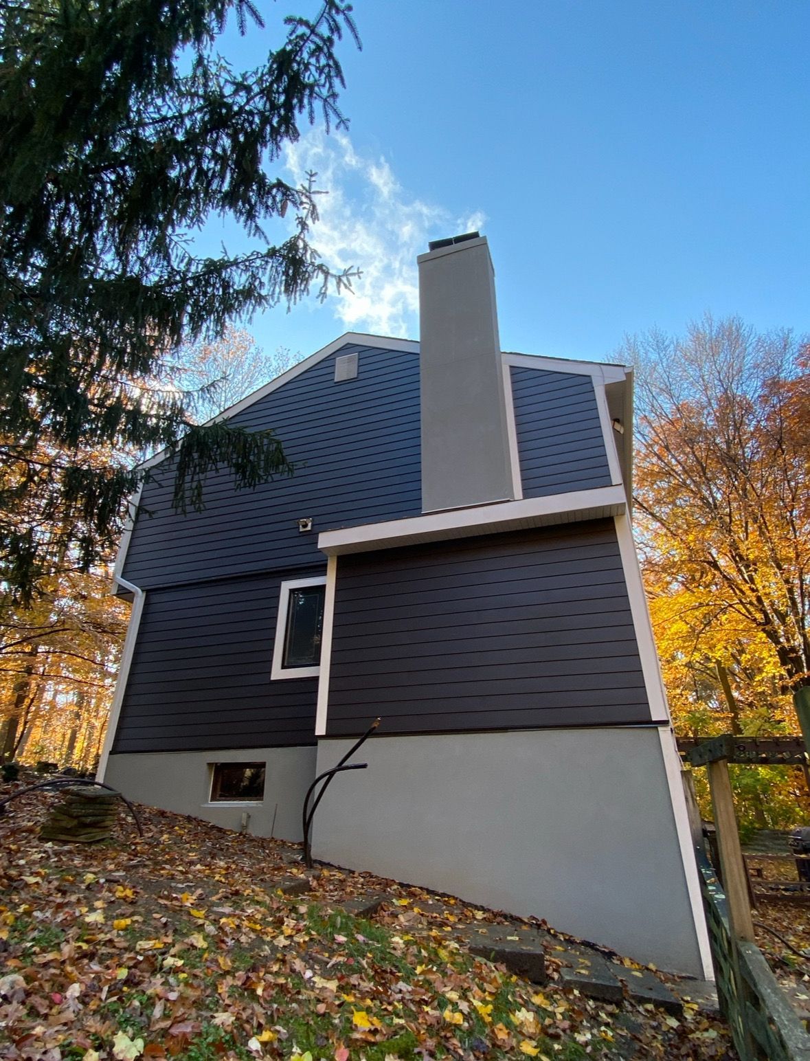 A house with a chimney on the side of it is surrounded by trees and leaves.