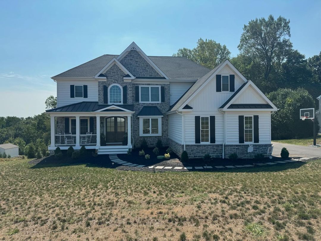 A large white house with black shutters is sitting in the middle of a field.