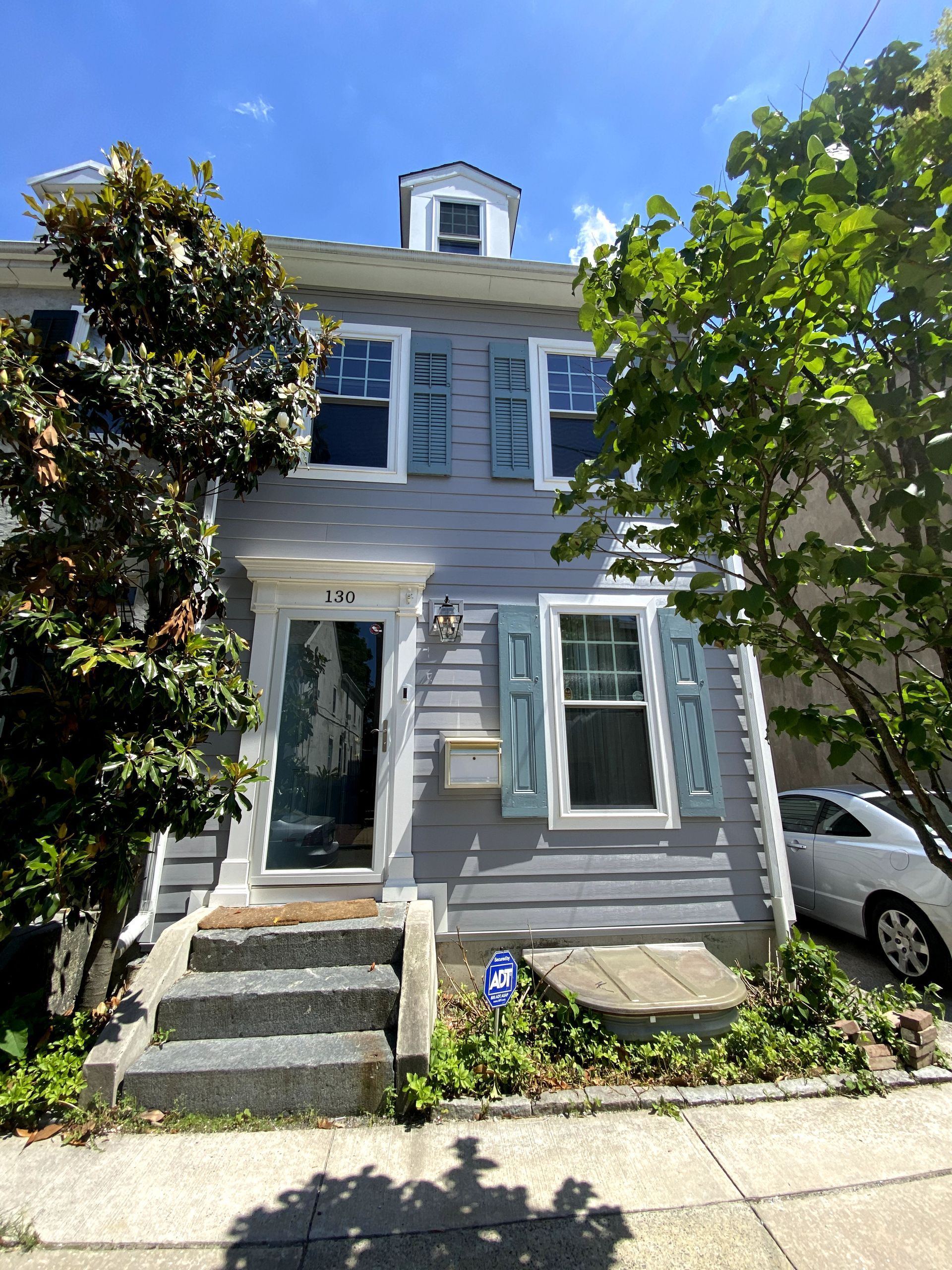 A gray house with blue shutters and a white car parked in front of it.