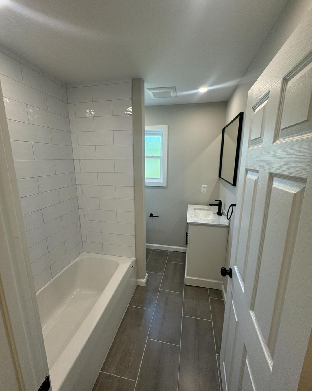 A bathroom with a tub , sink , mirror and window.