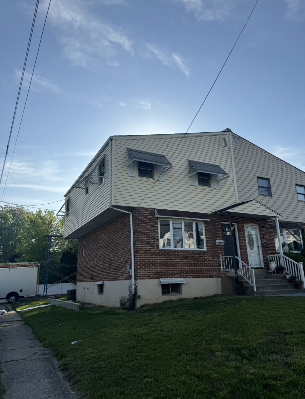 A brick house with a white siding and black awnings on the windows.