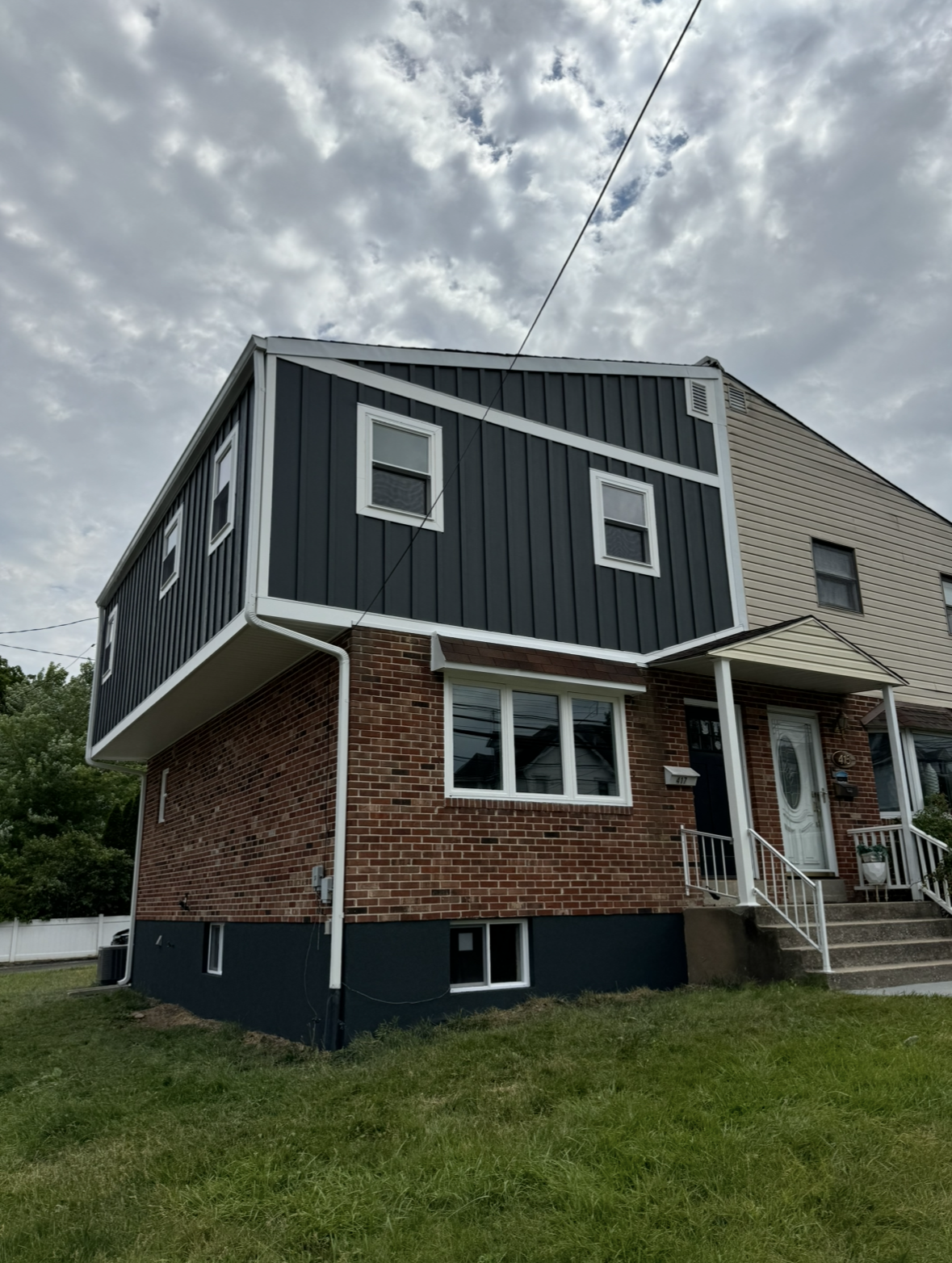 A brick house with a black siding and white trim is sitting on top of a lush green hillside.