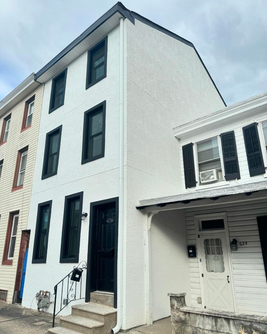 A white building with black shutters is next to another white building.