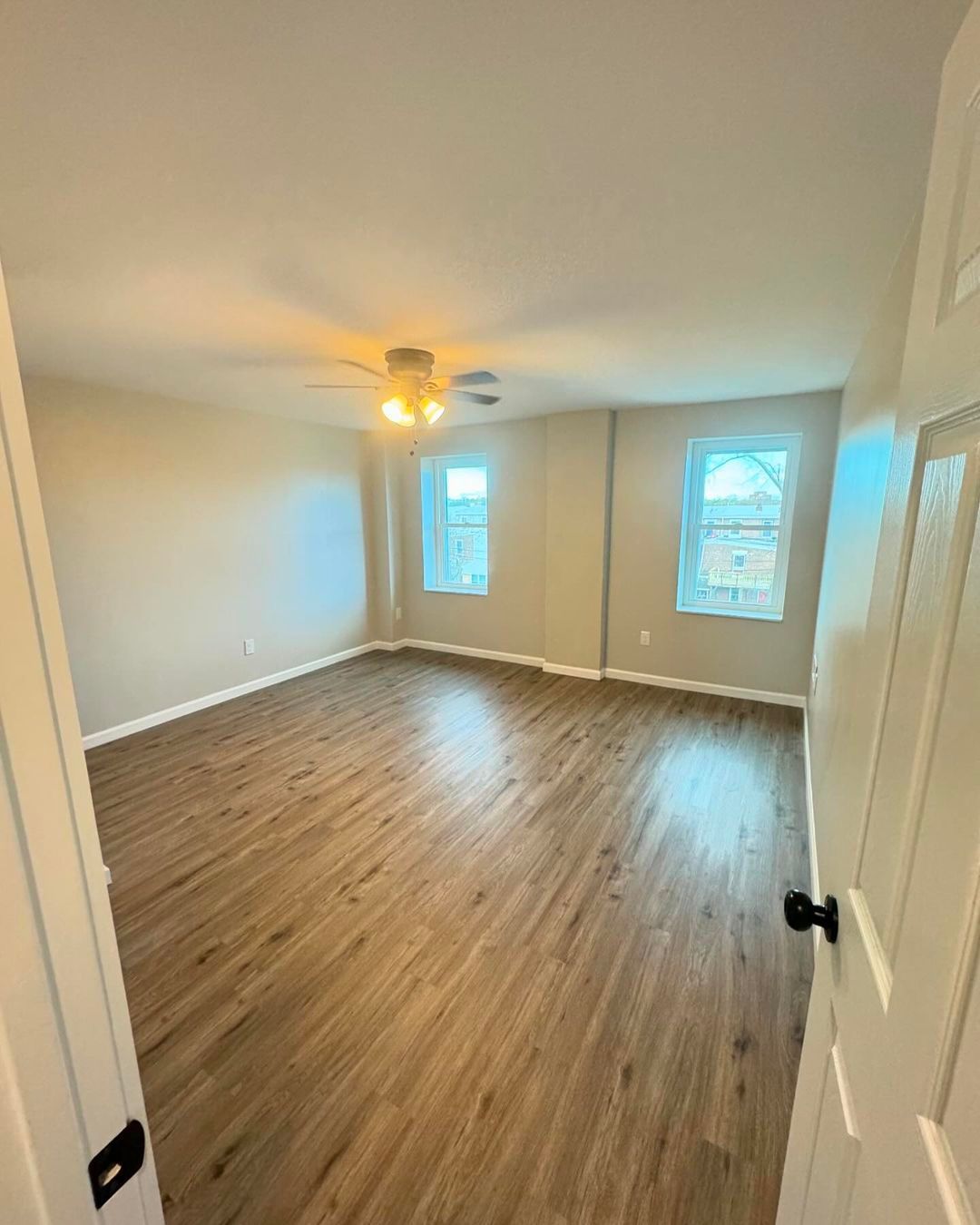 A large empty room with hardwood floors and a ceiling fan.