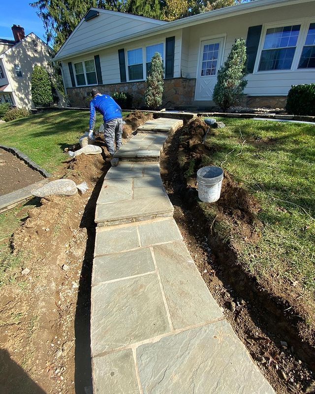 A man is working on a stone walkway in front of a house.