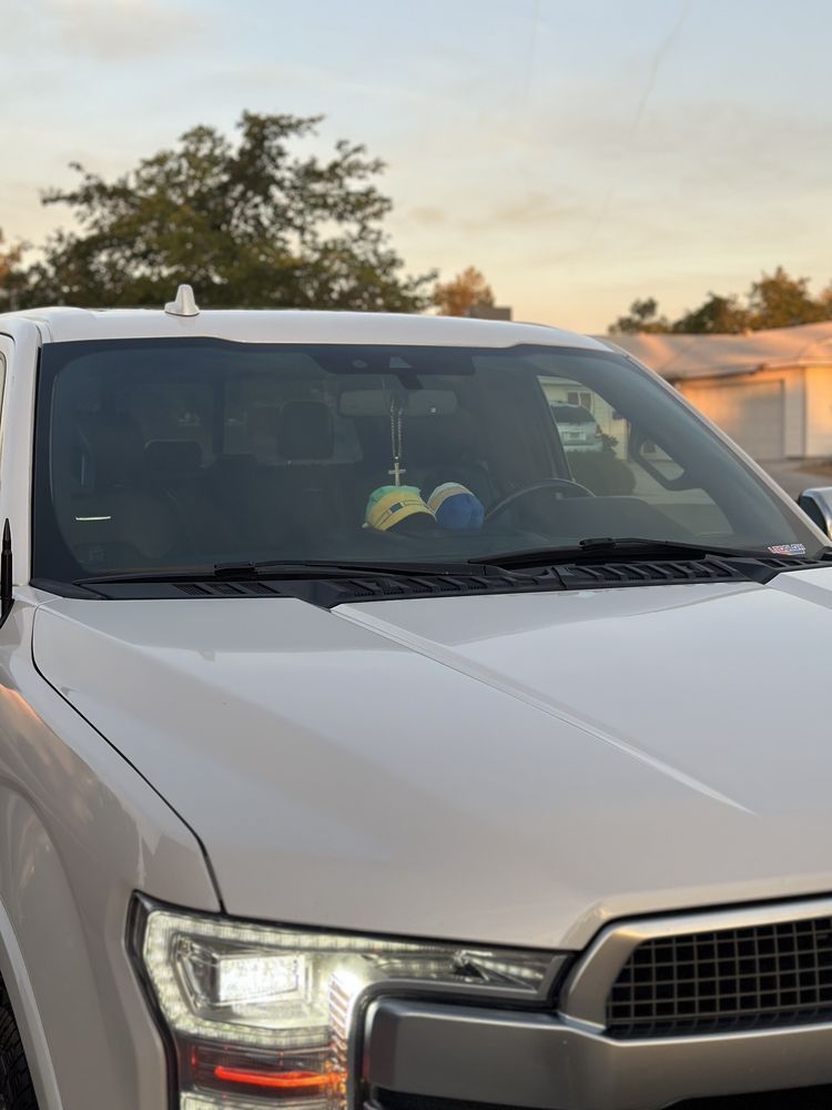 White pickup truck, front view, windshield with two small hanging decorations, sunset in background.