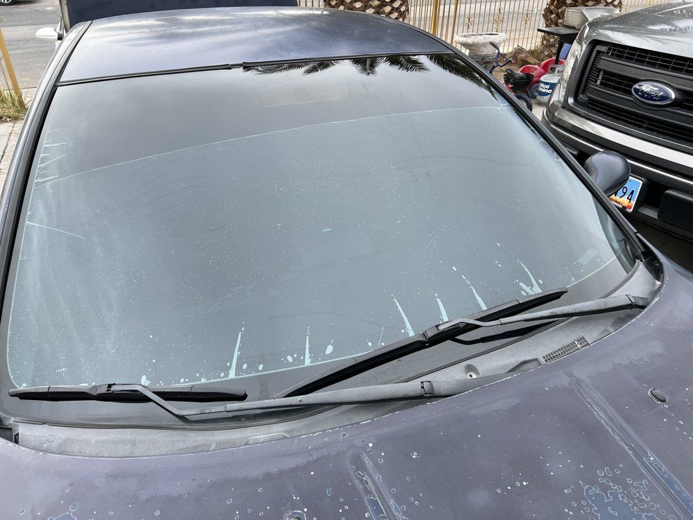 Blue car with dirty windshield and wipers, parked outside.