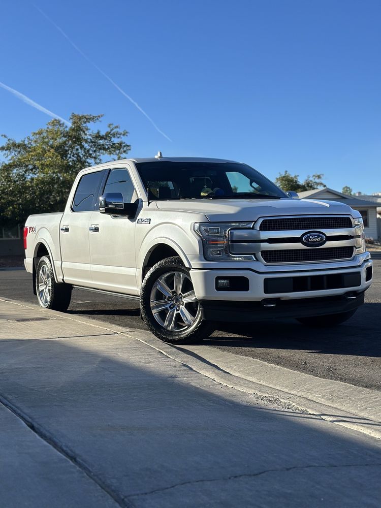 White Ford F-150 truck parked on a paved driveway in sunny weather.