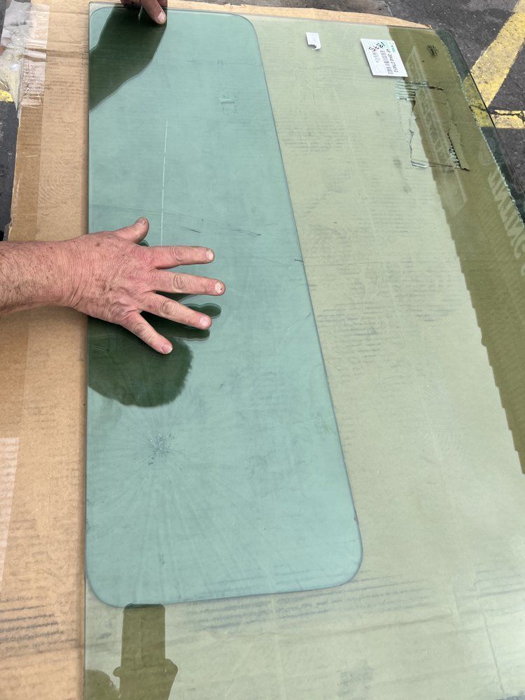 Person's hand touching a long, light green glass pane. A cardboard box is visible in the background.