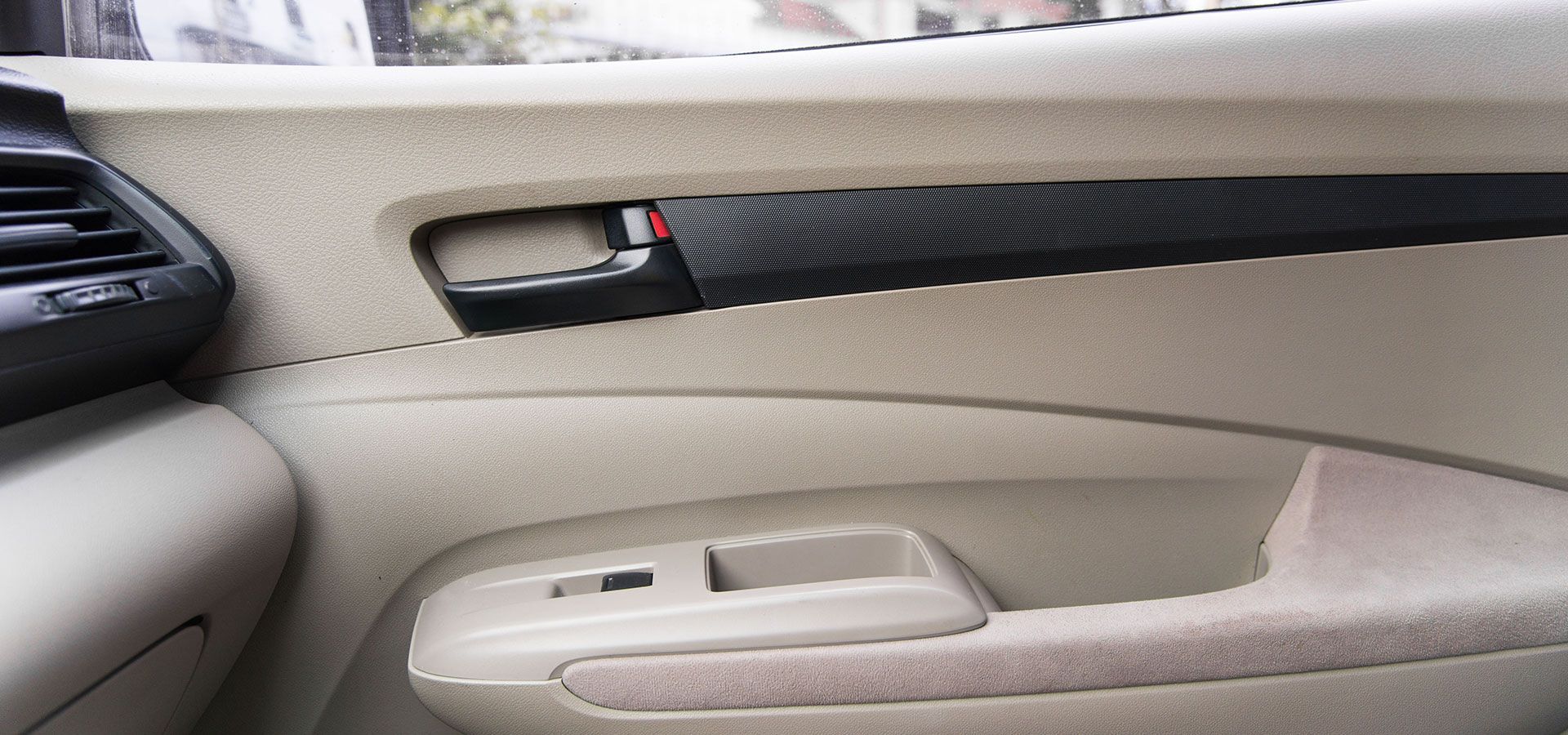 Beige car door interior with black accents, handle, and window controls.