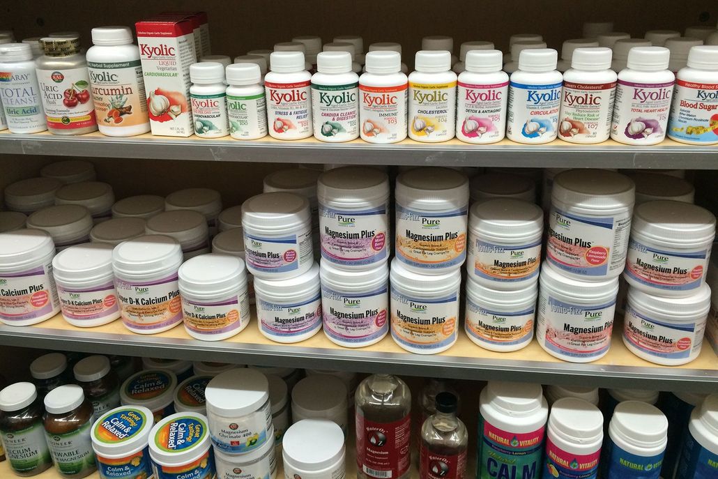 Shelves stocked with various white supplement jars and small bottles of liquids, brightly labeled.