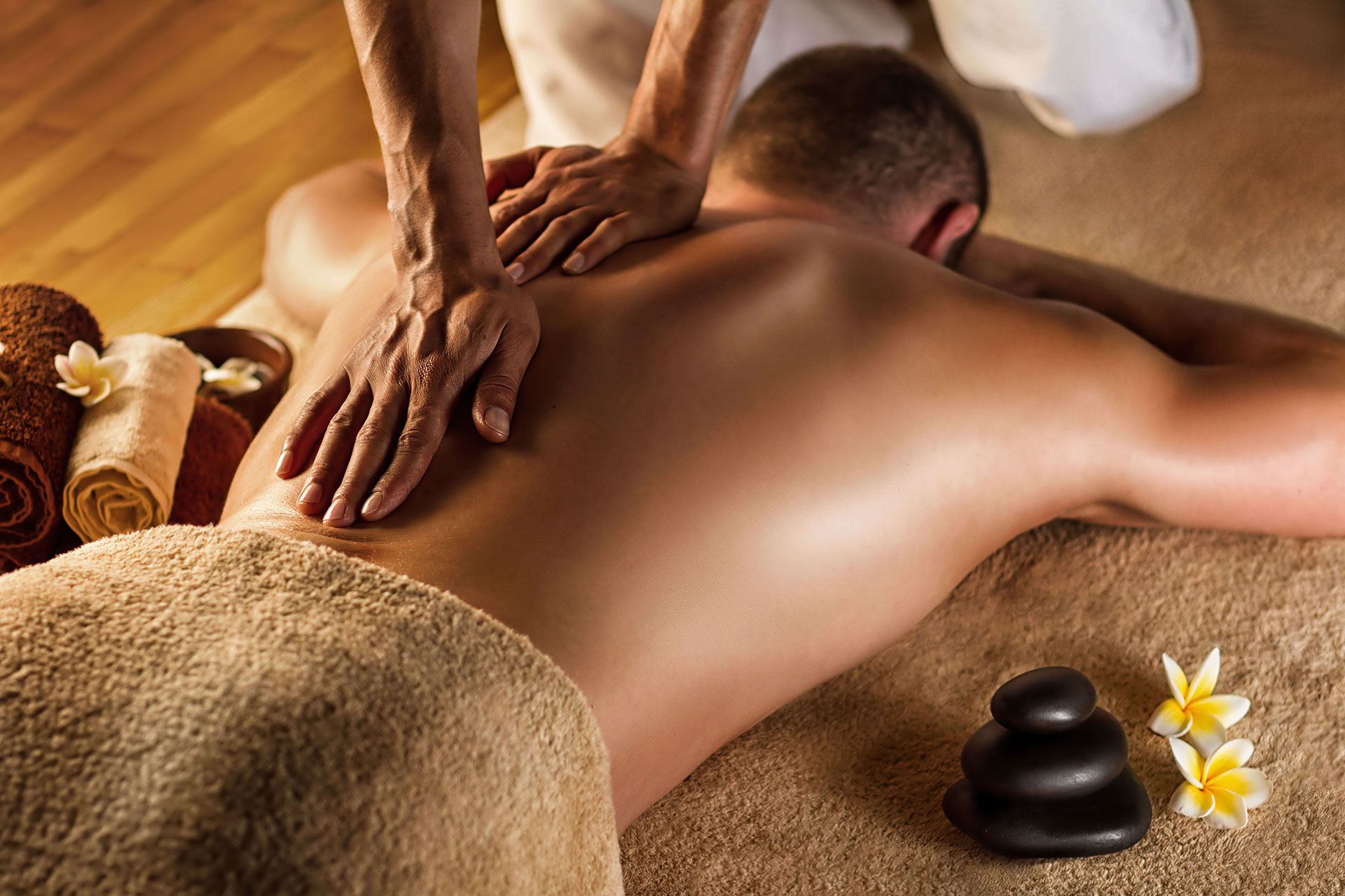Man receiving back massage, lying on a massage table. Therapist's hands are on the man's back.