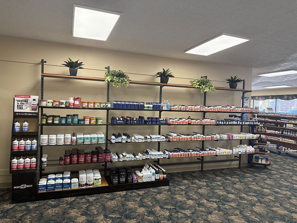 Shelves stocked with supplements in a retail store. Dark shelving, products displayed, decorative plants, and carpeted floor.