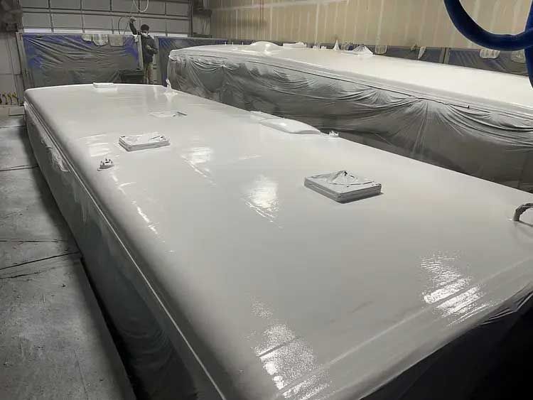 A white boat is being painted in a paint booth.