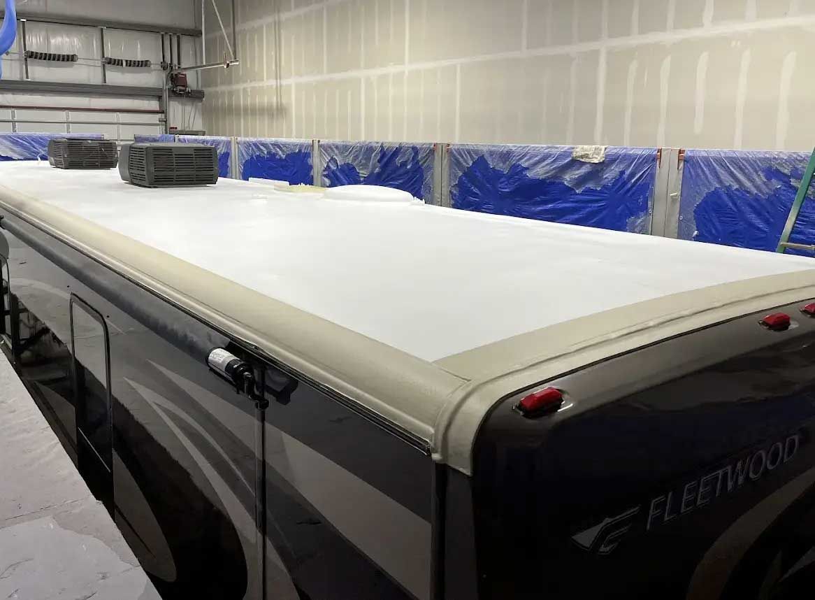 A rv with a white roof is sitting in a garage.