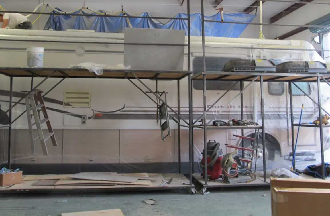 A rv is being painted in a garage with scaffolding
