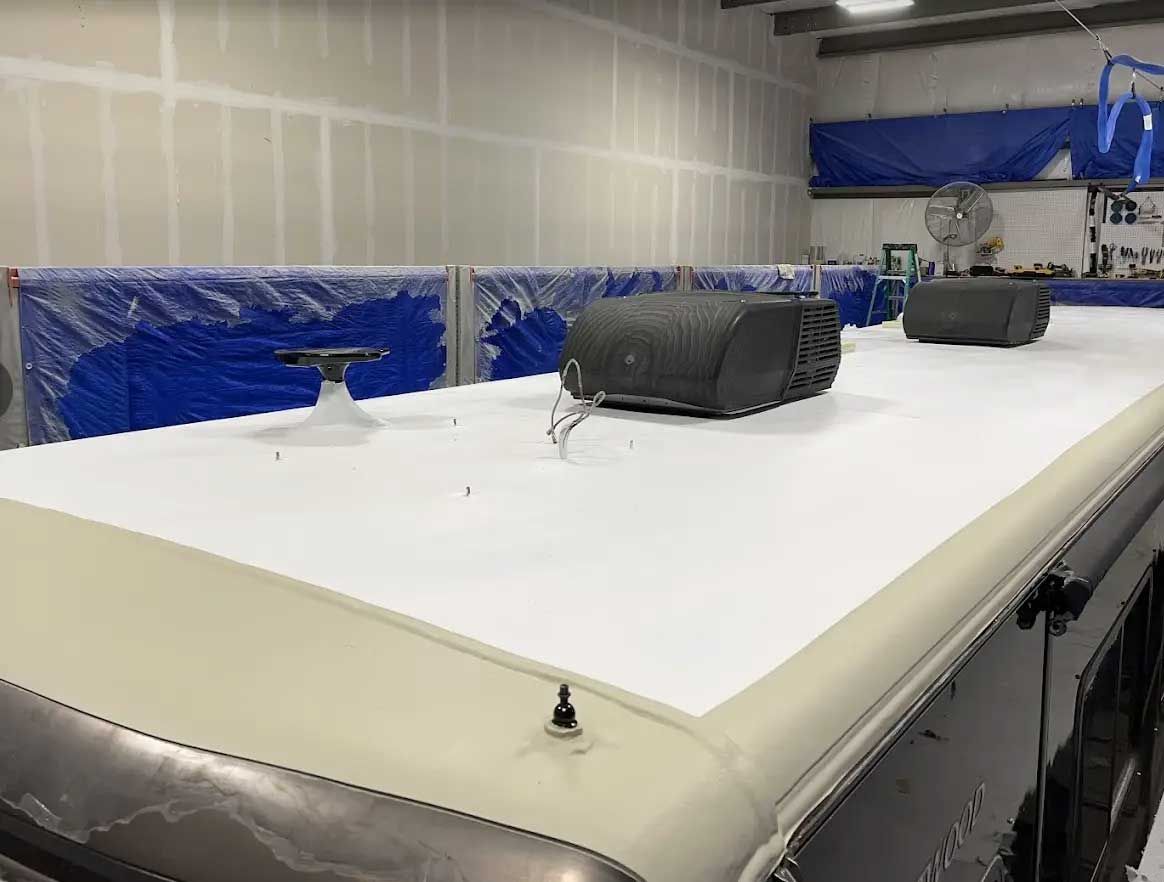 A roof of a camper is being painted in a garage.