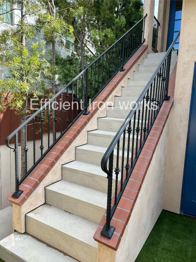 Outdoor staircase with black iron railings and red brick trim, leading up to a building with a blue door.