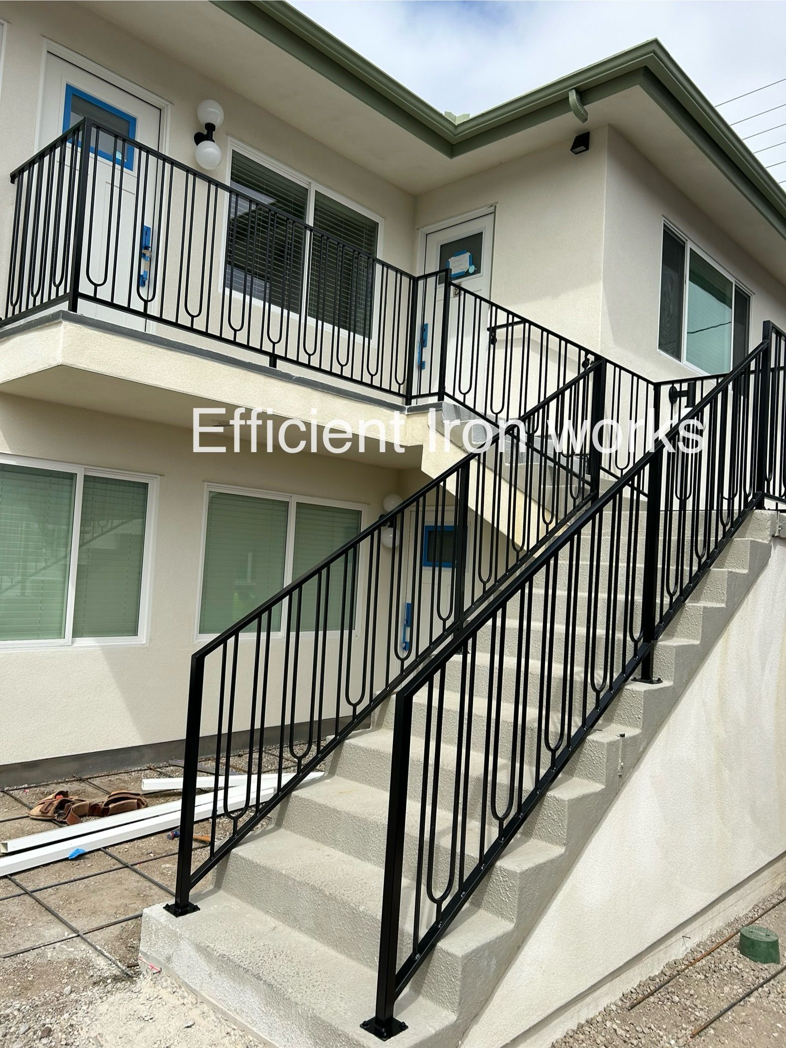 Black metal stair railings and balcony railings on a two-story building with light-colored stucco walls.