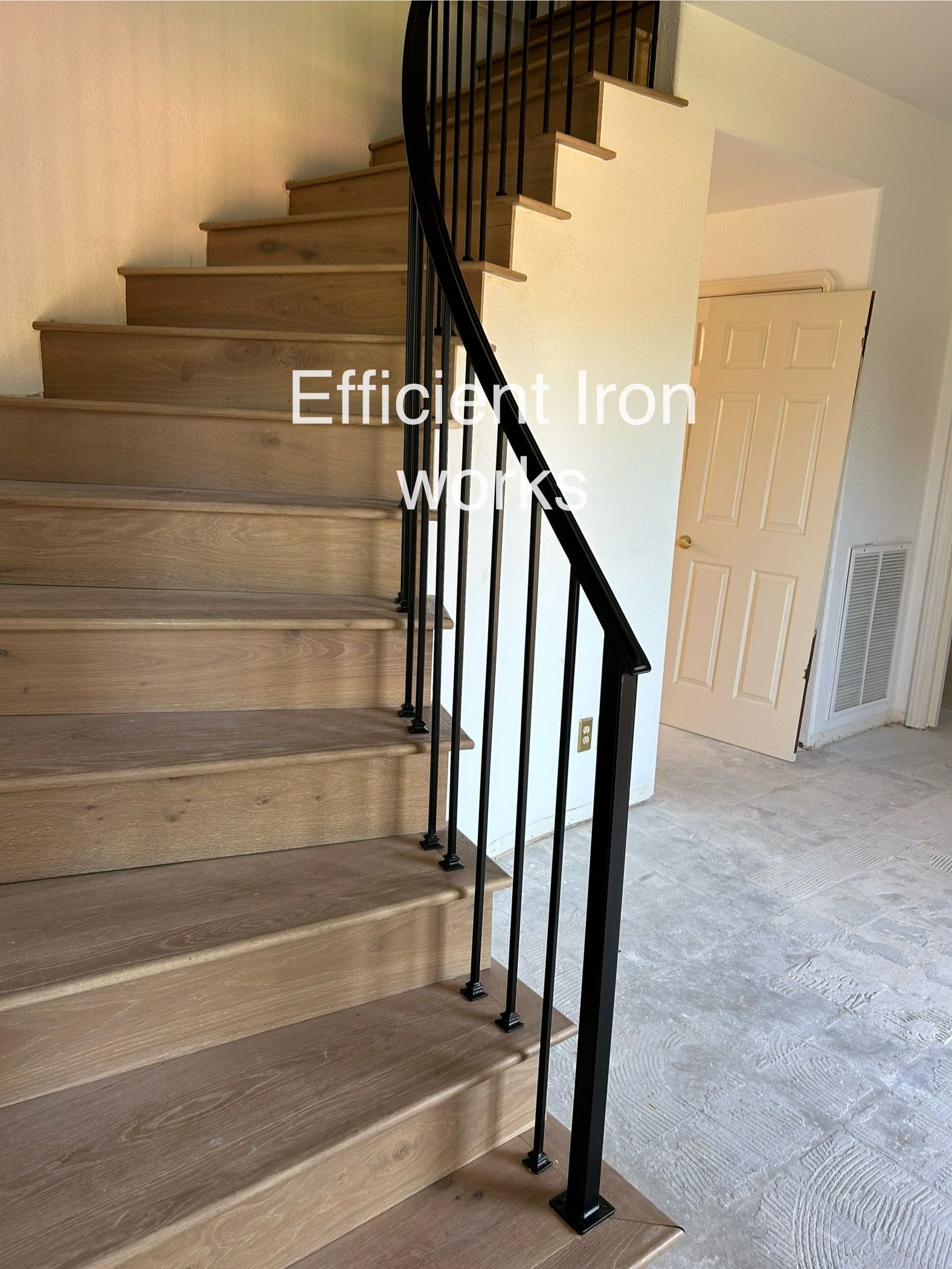 A curved wooden staircase with black iron railings. The staircase leads upward into a well-lit interior.
