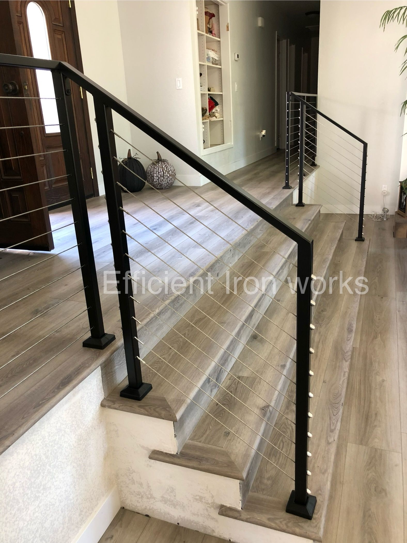 Black metal handrails with cable infill on a set of indoor steps with light wood-look flooring.