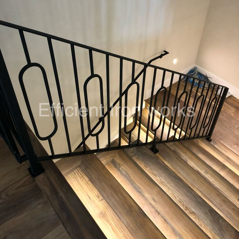Black metal railing with a unique oval design on a wooden staircase.