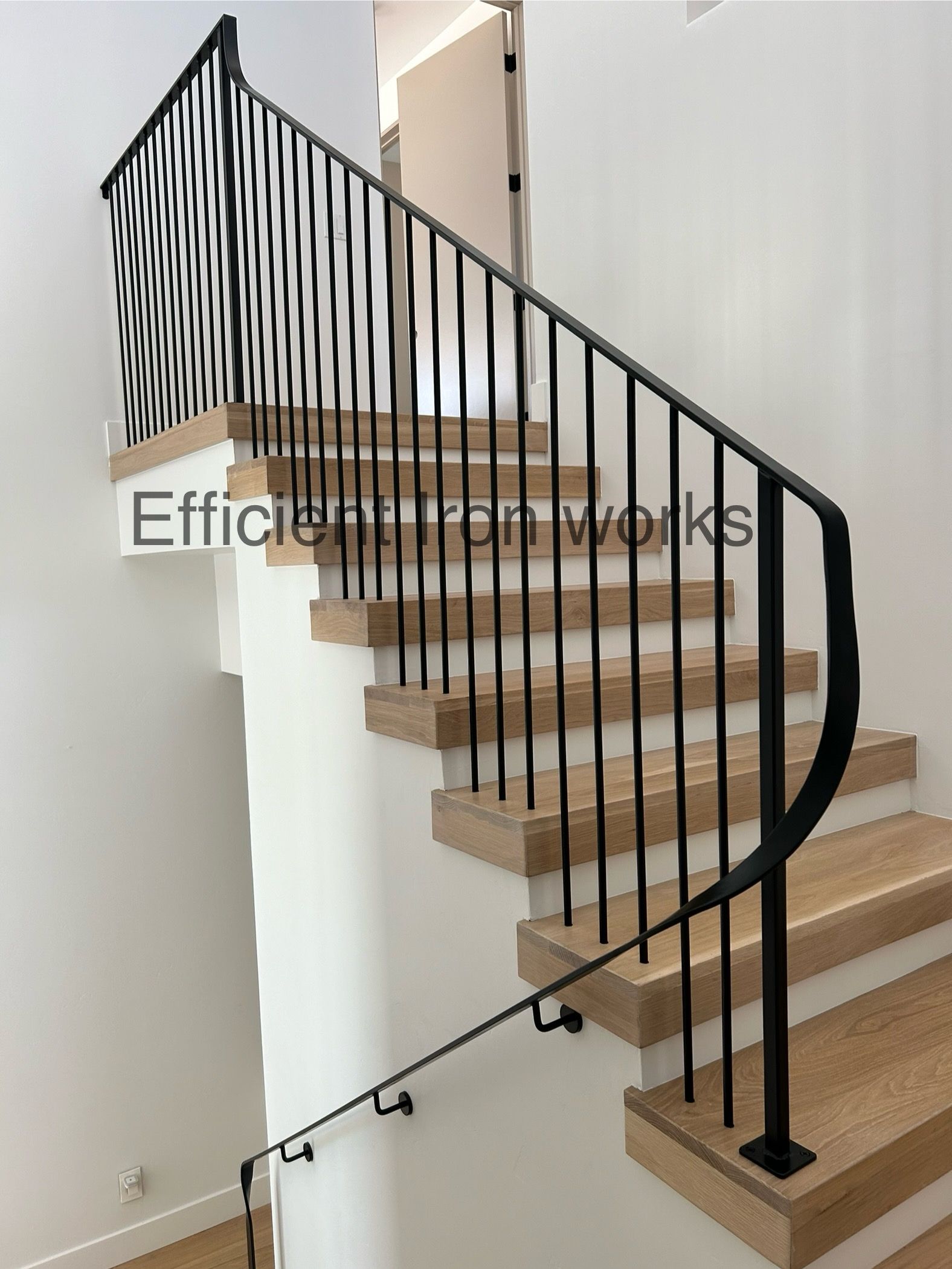 Black iron staircase railing with vertical bars on a wooden staircase with white walls.