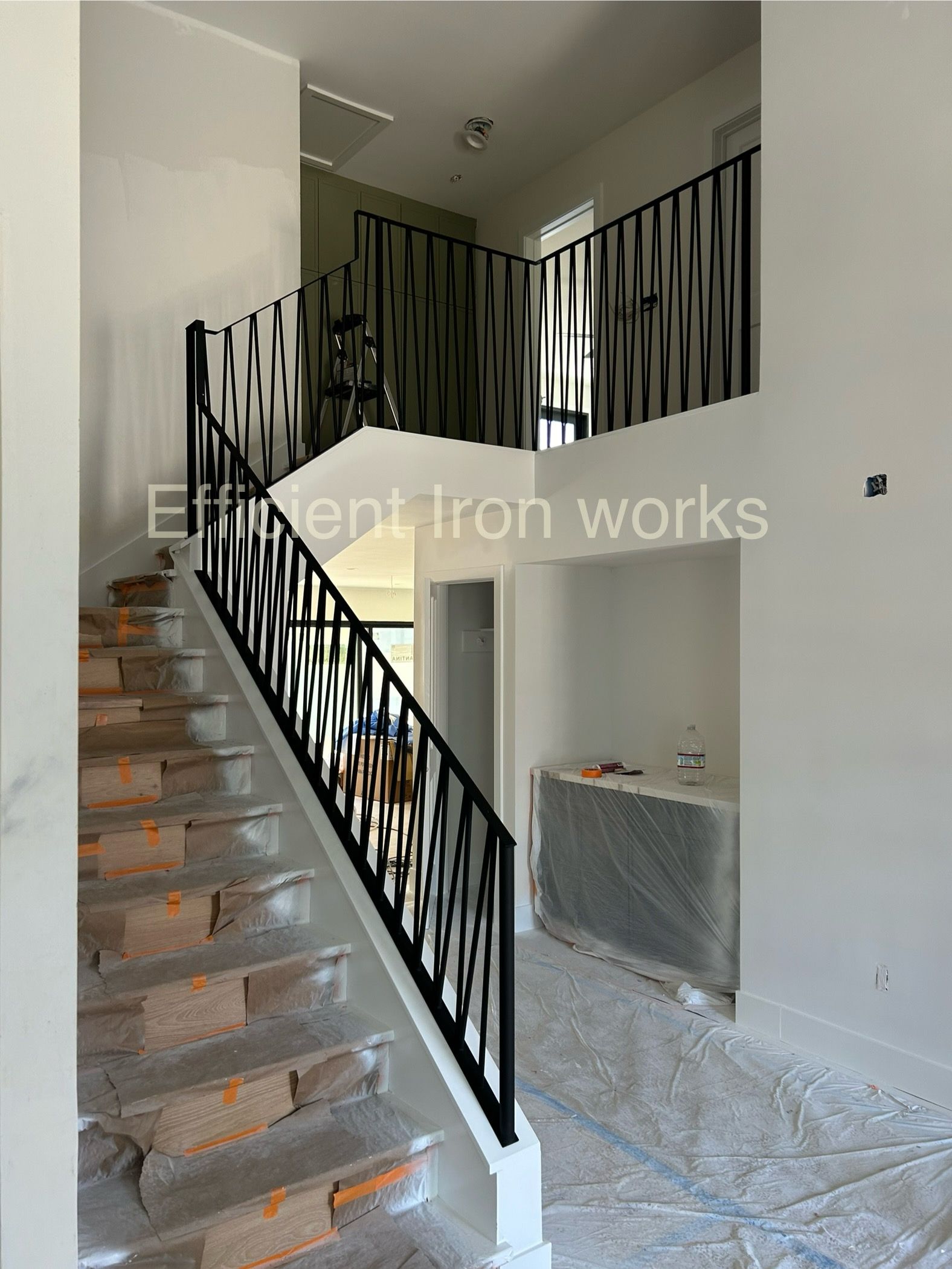 A staircase with black iron railing that has a wavy design. The stairs are unfinished brick and lead to a landing with more of the railing.